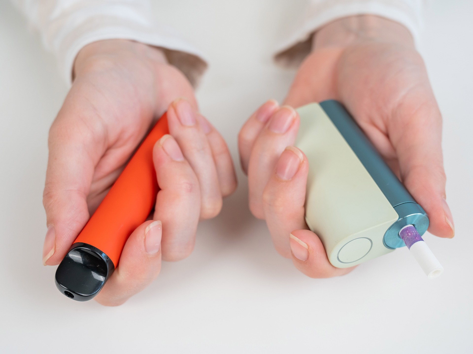 Woman holding electronic cigarette and disposable vape on white background. Tobacco heating systems and vaporizer.